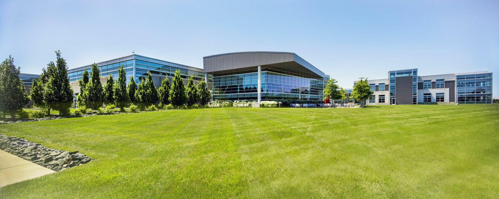 Modern glass building with green lawn and trees.