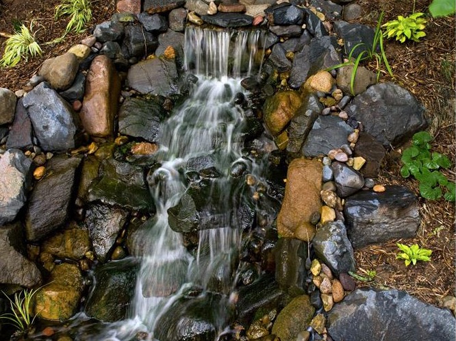 Small garden waterfall with rocks and plants.