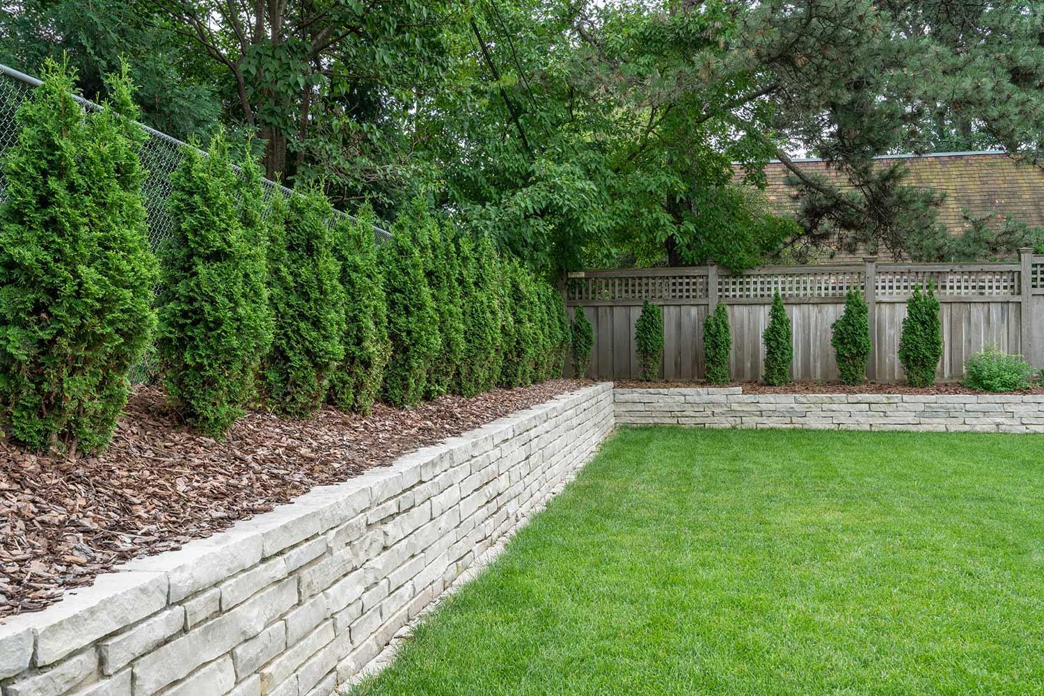 Hedges and a mortared limestone retaining wall create a privacy border for this backyard in Edina, MN