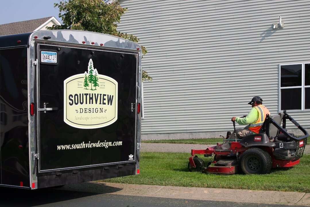 Landscape contractor mowing grass near trailer.