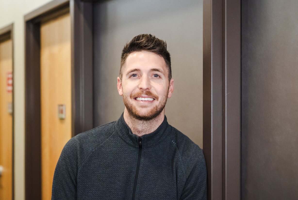 Smiling man standing in hallway, wearing sweater.