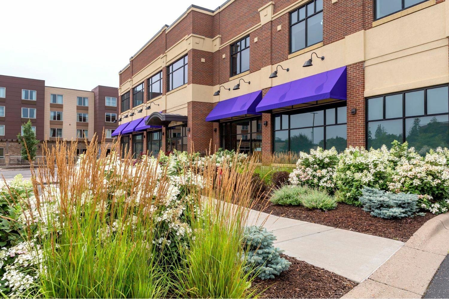 Modern building with purple awnings and landscaped garden.