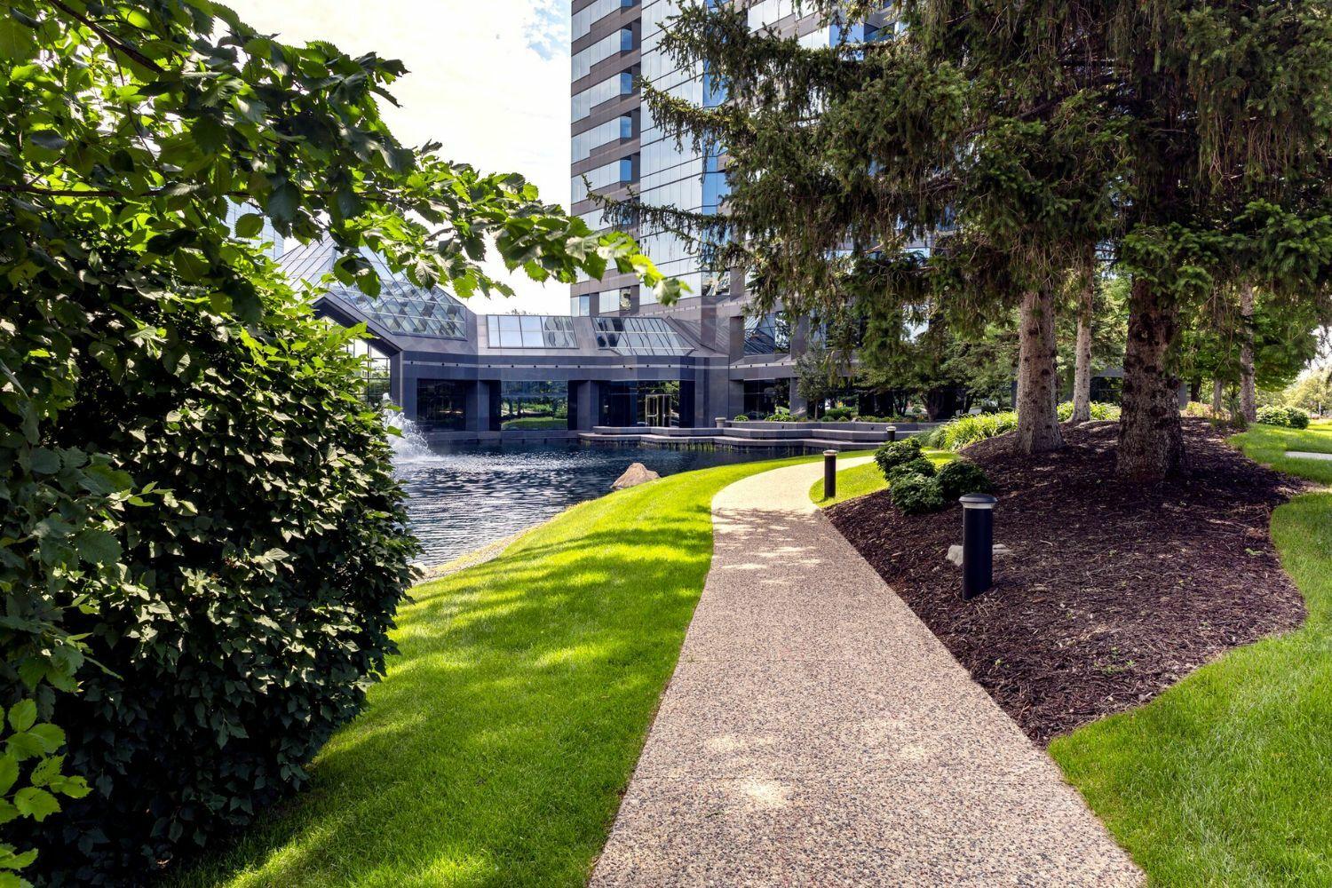 Pathway by pond near modern building with greenery.
