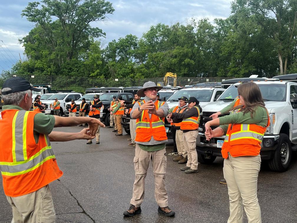 Workers in safety vests stretching near trucks.