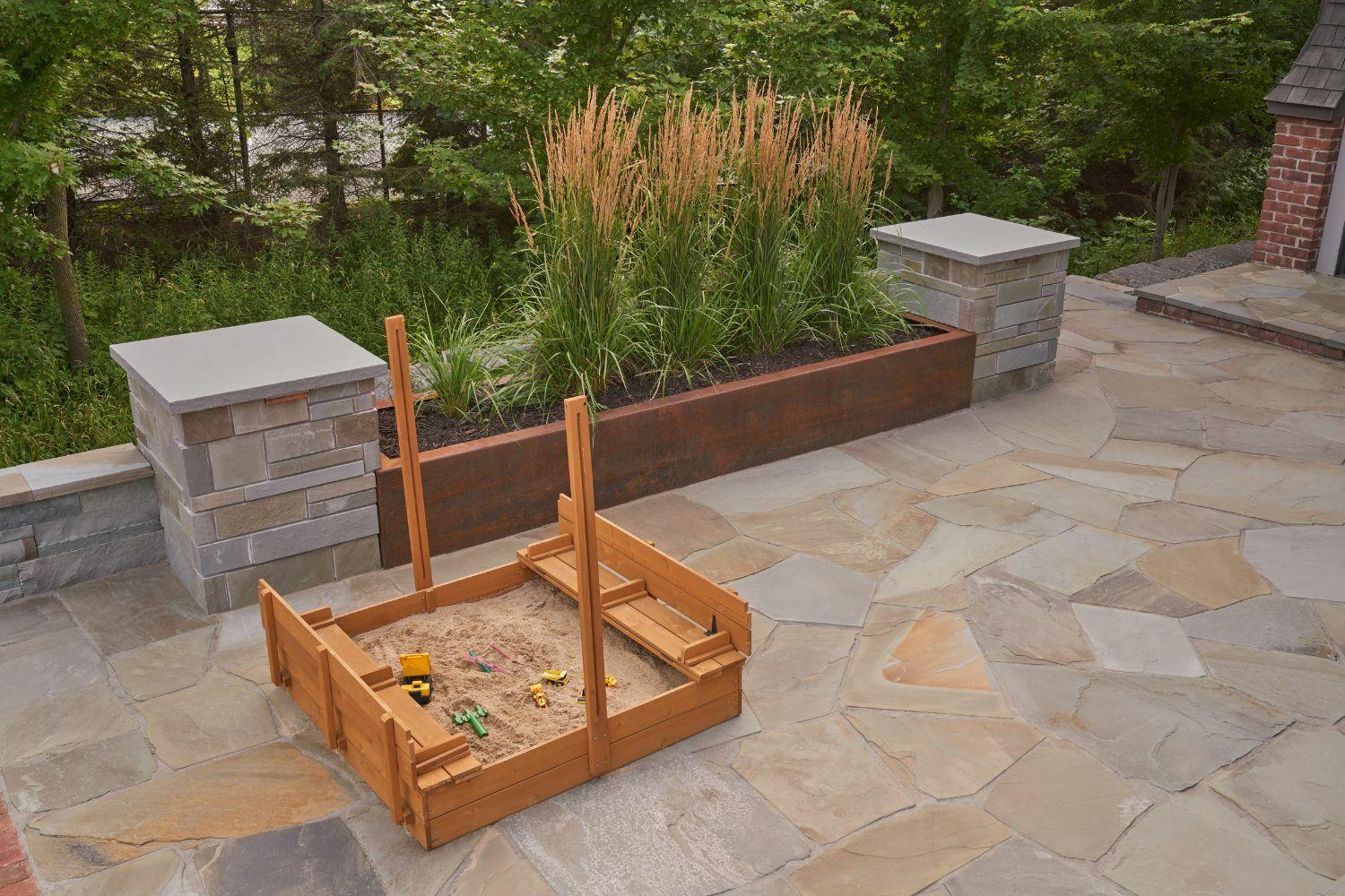 Wooden sandbox on stone patio with plants.