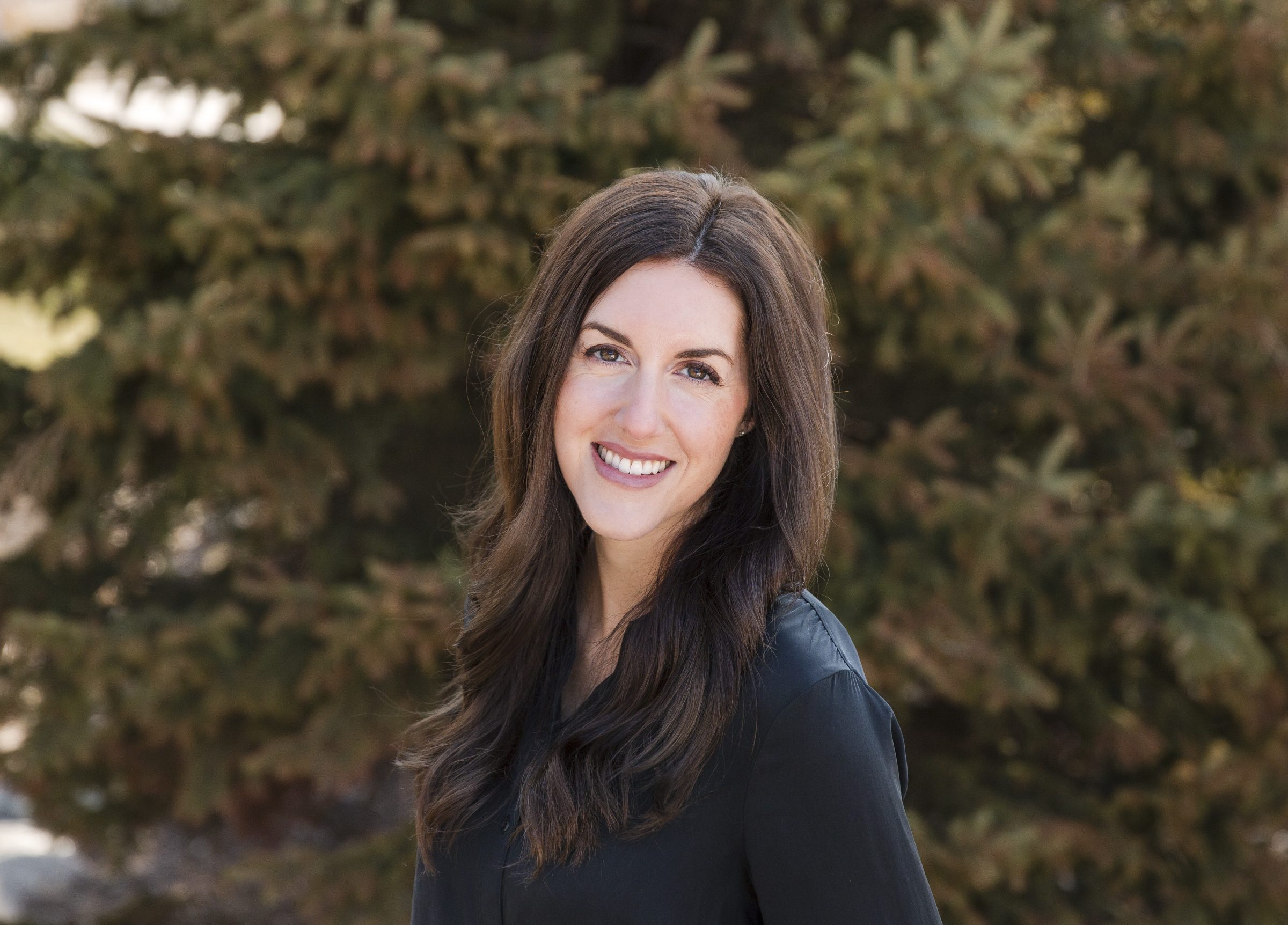 Smiling woman outdoors with background greenery.
