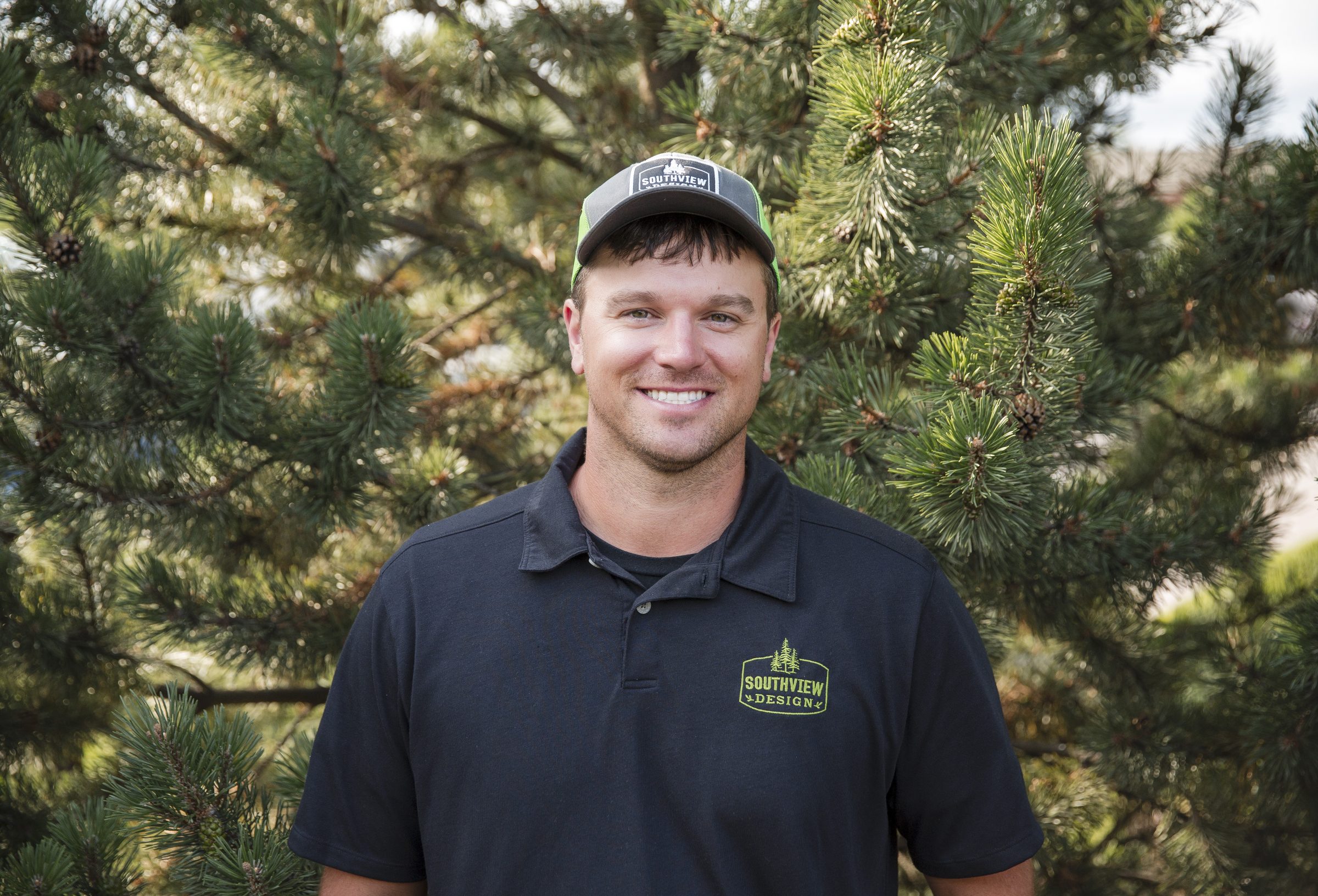 Man in cap smiling by pine tree