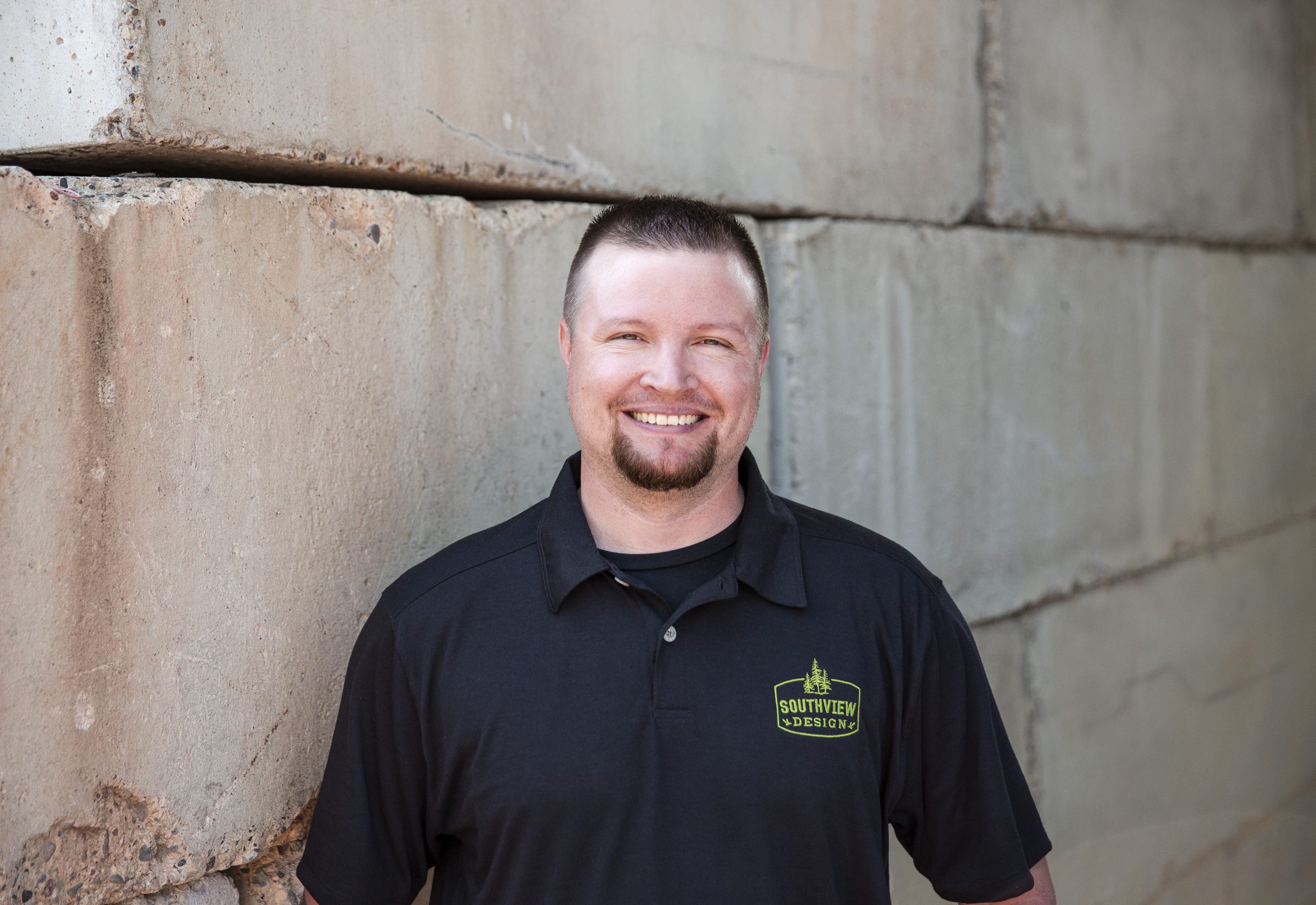 Smiling man in Southview Design shirt by concrete wall.
