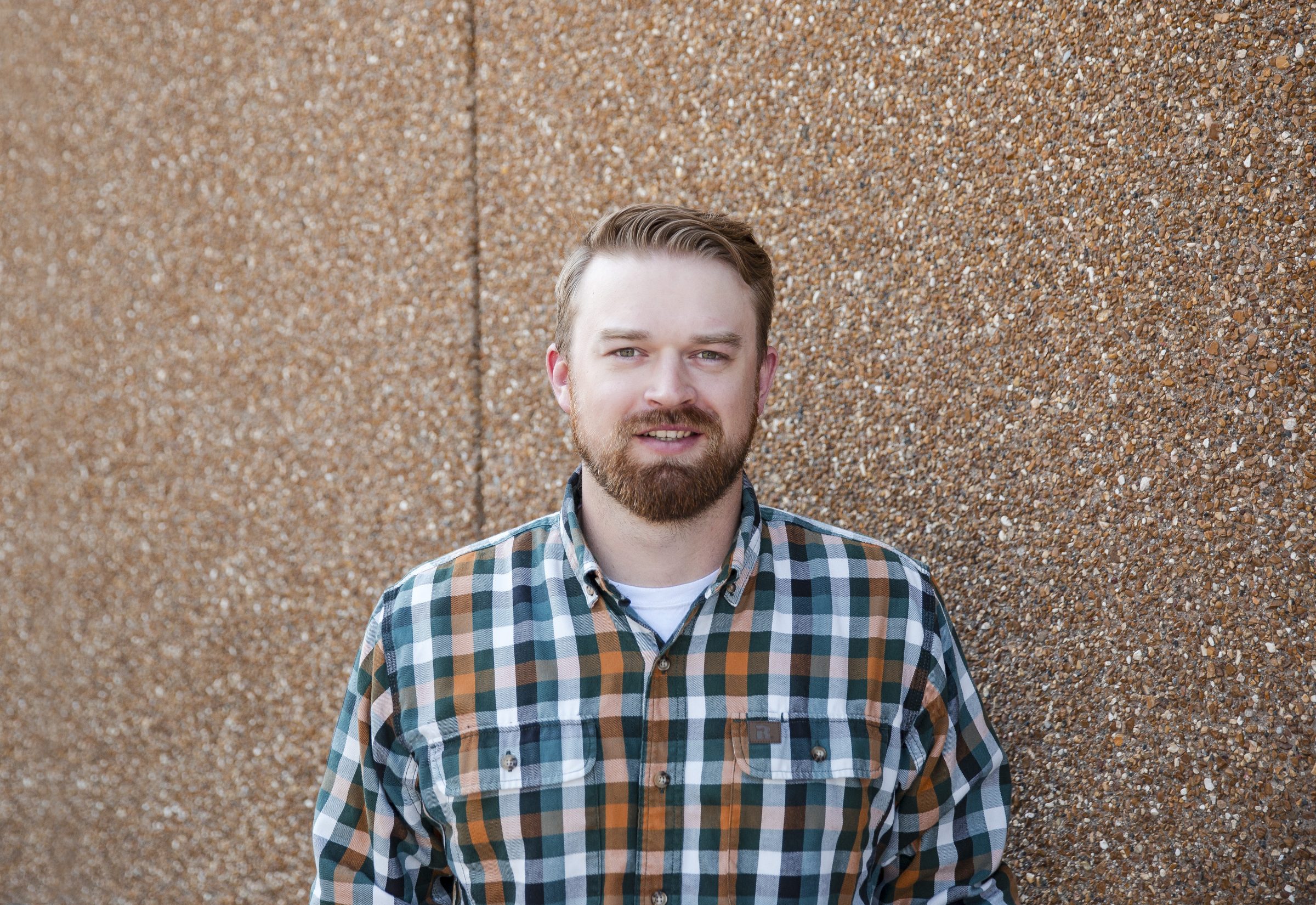 Man in plaid shirt against textured wall background.