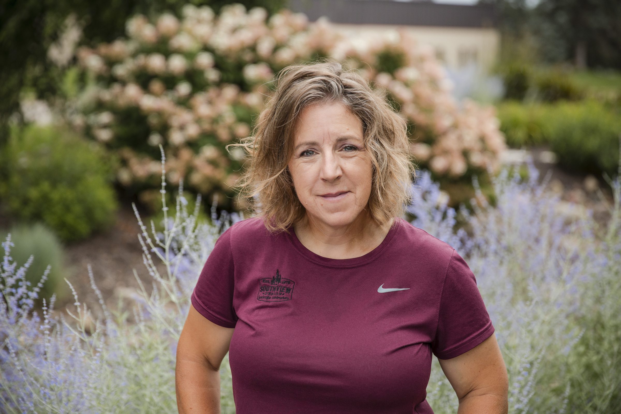 Woman in garden wearing maroon shirt.