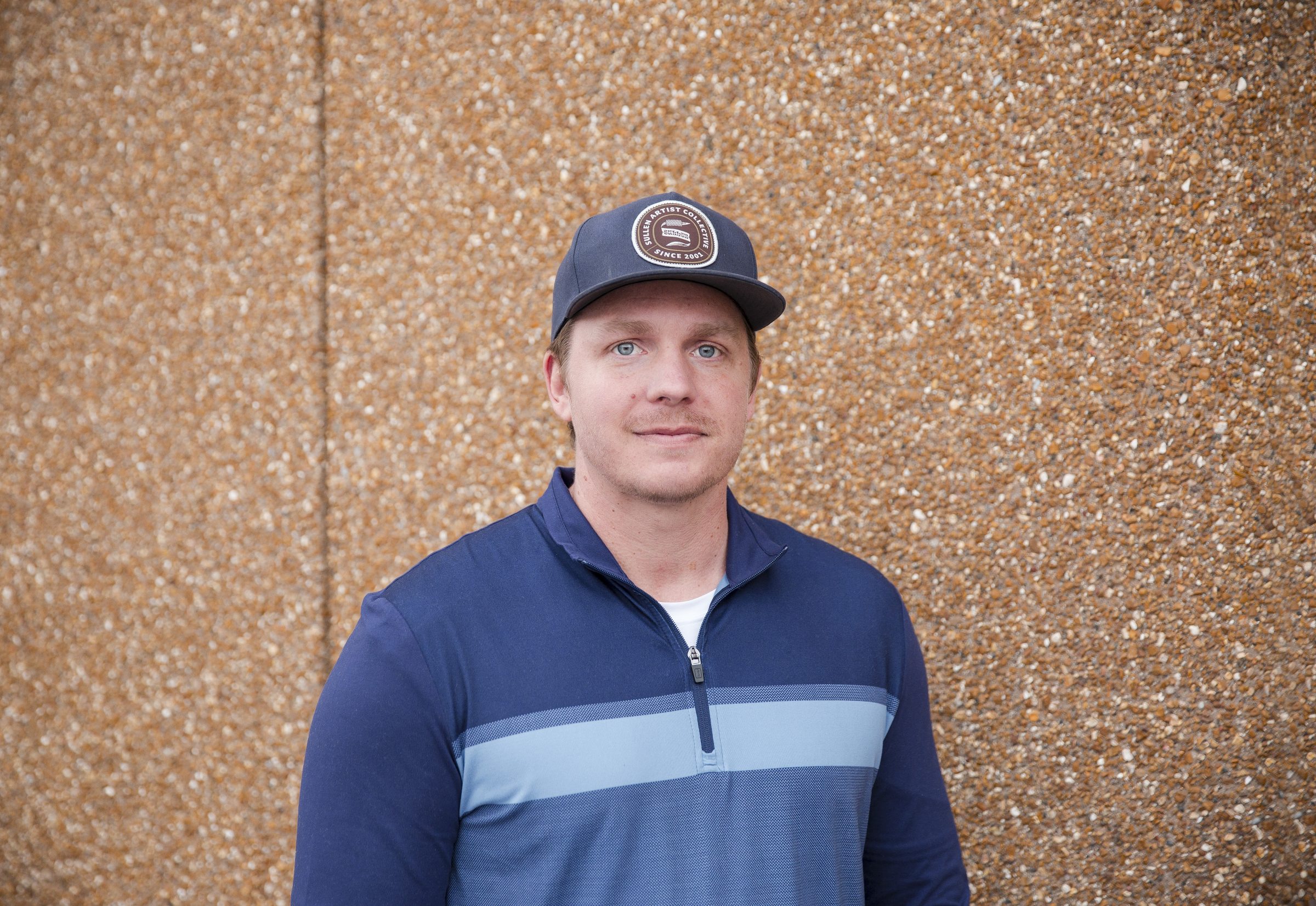 Man wearing blue jacket and cap against textured wall