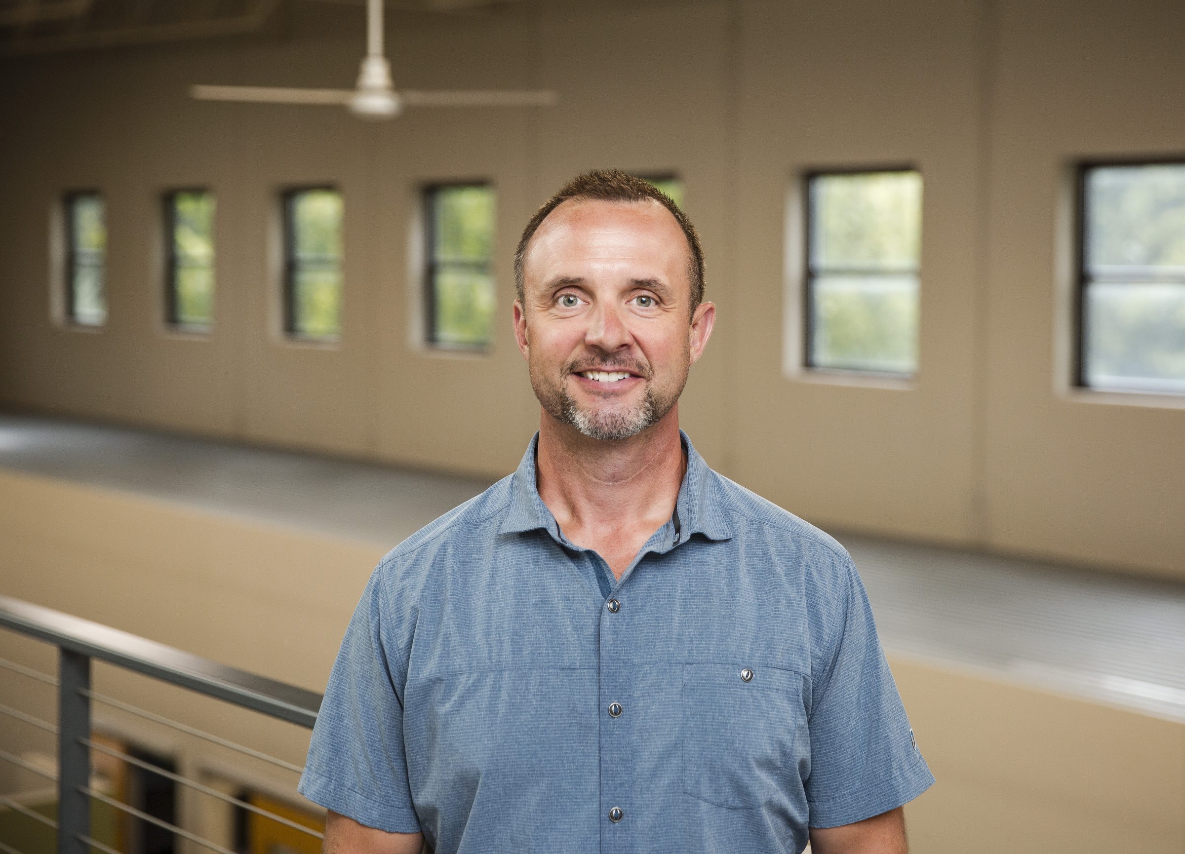 Smiling man in office hallway with windows.