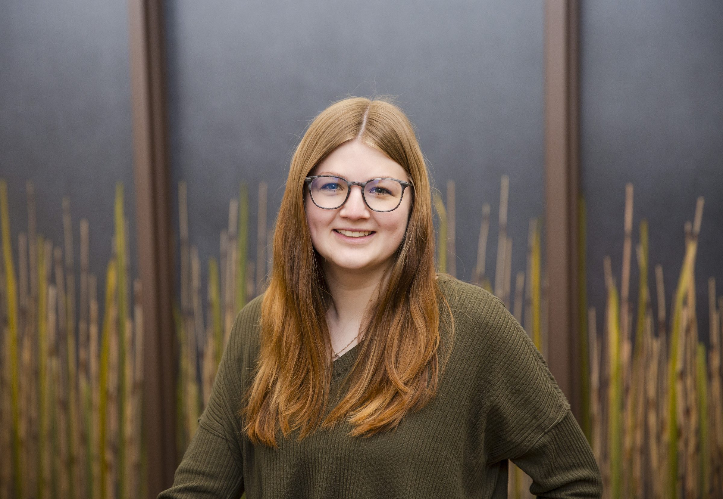 Person smiling with long hair and glasses.