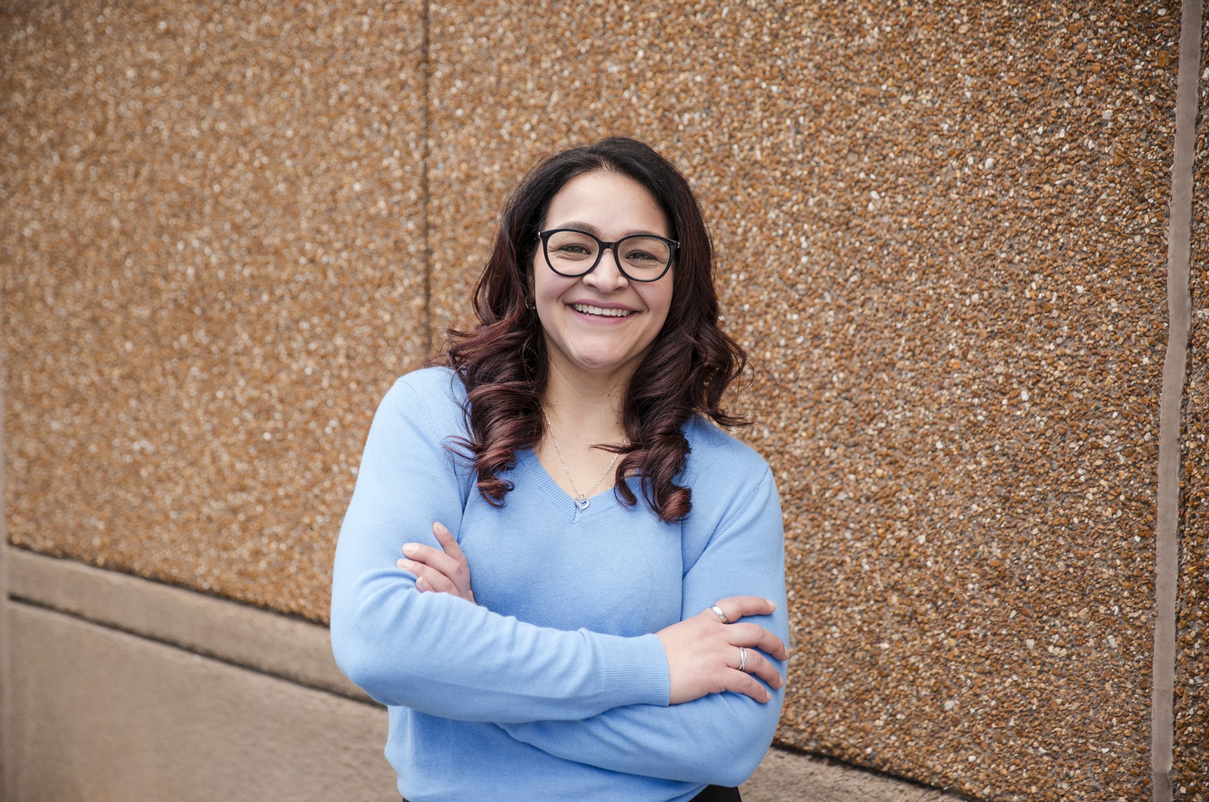 Smiling person with glasses, blue sweater, arms crossed.