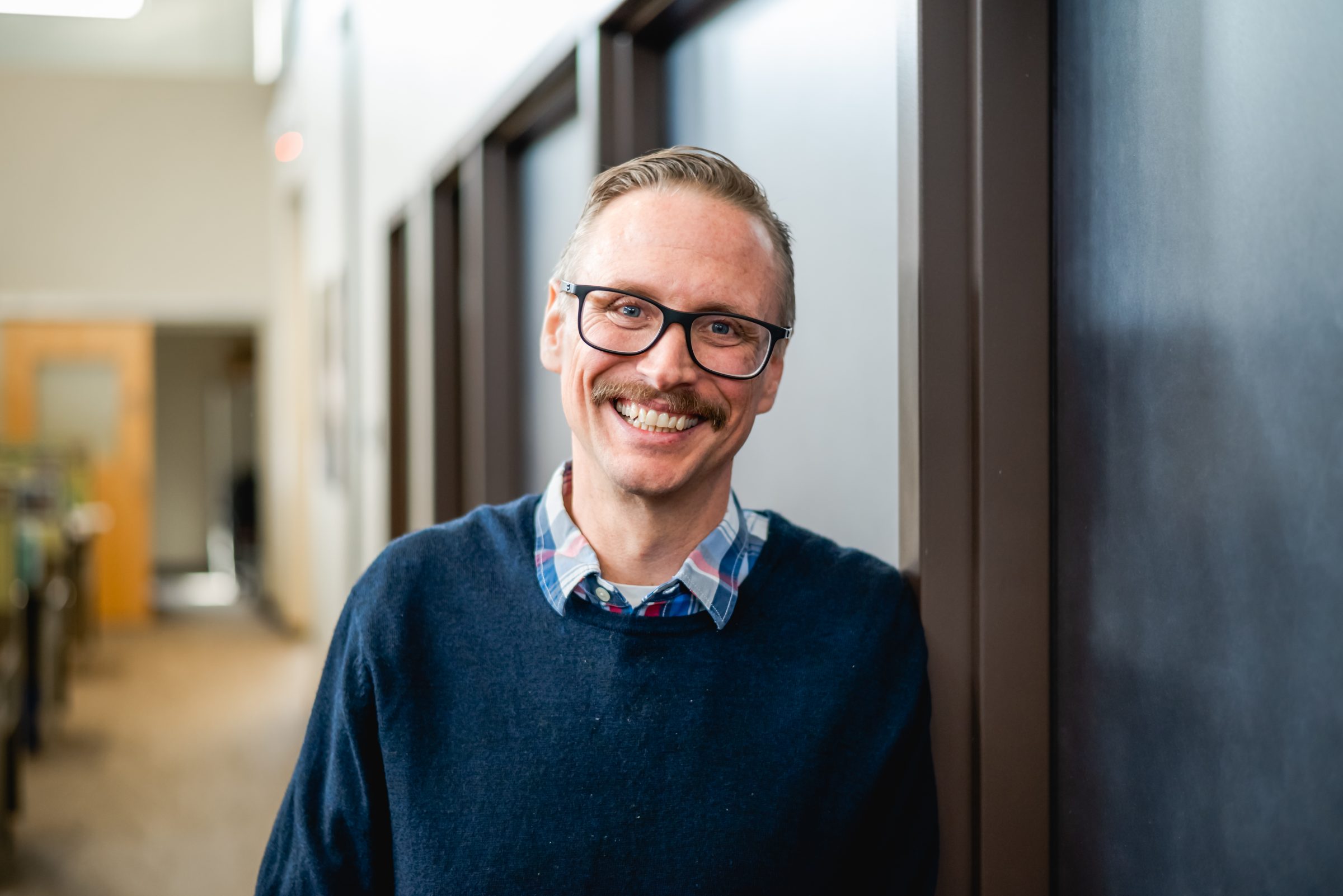Smiling person with glasses in office hallway
