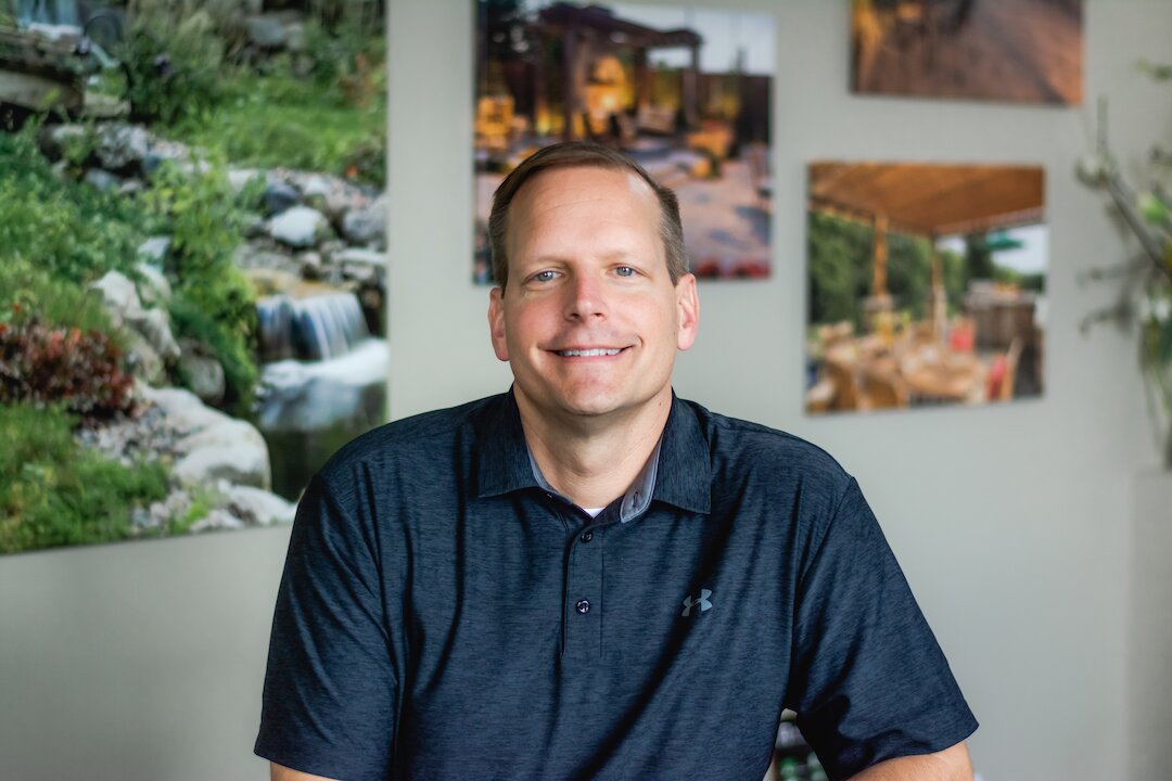 Man smiling in front of landscape photographs.
