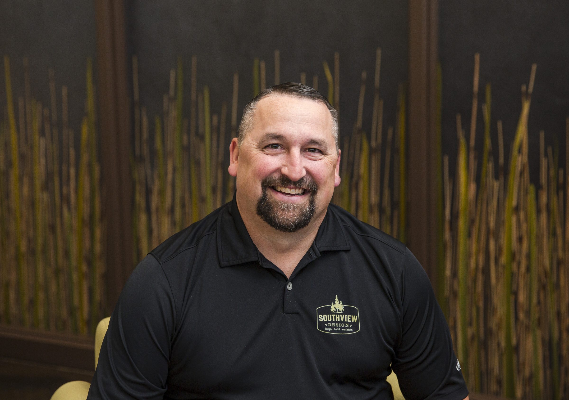 Smiling man in black shirt with bamboo background.