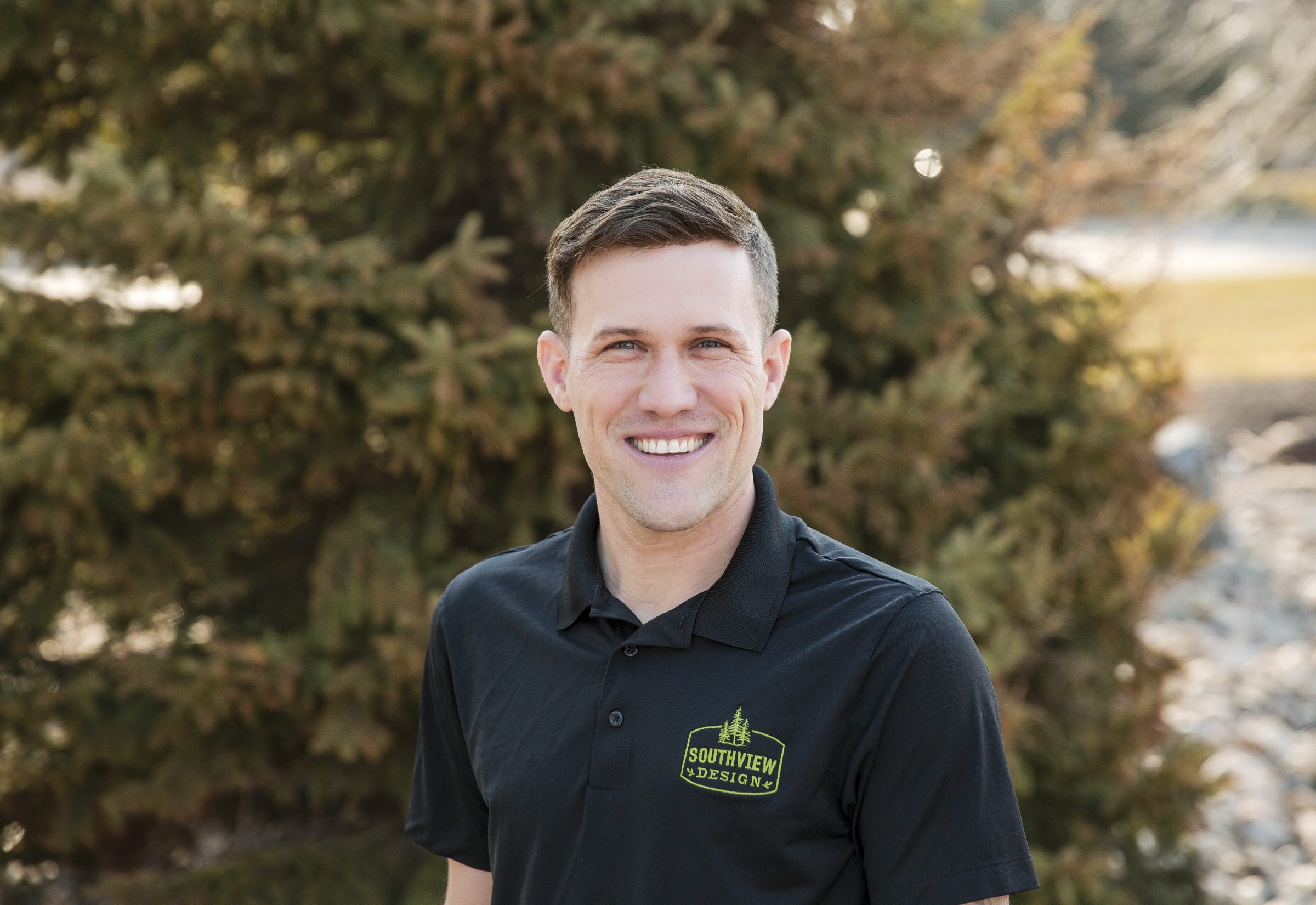 Man smiling outdoors in black polo shirt.