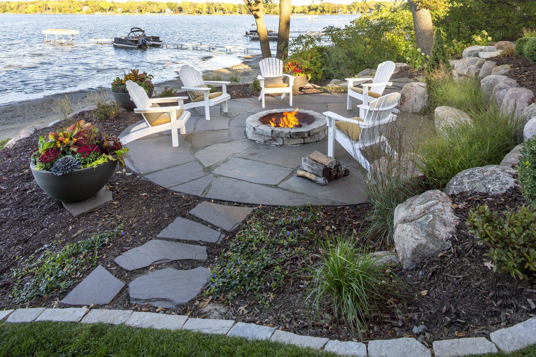 Circular flagstone fire pit patio with Adirondack chairs and boulder landscaping on a lakeshore