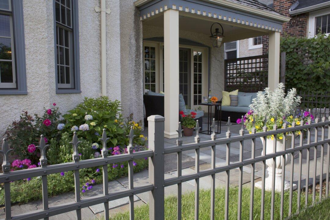 Covered front porch with flagstone patio, colorful garden beds, and decorative iron fence