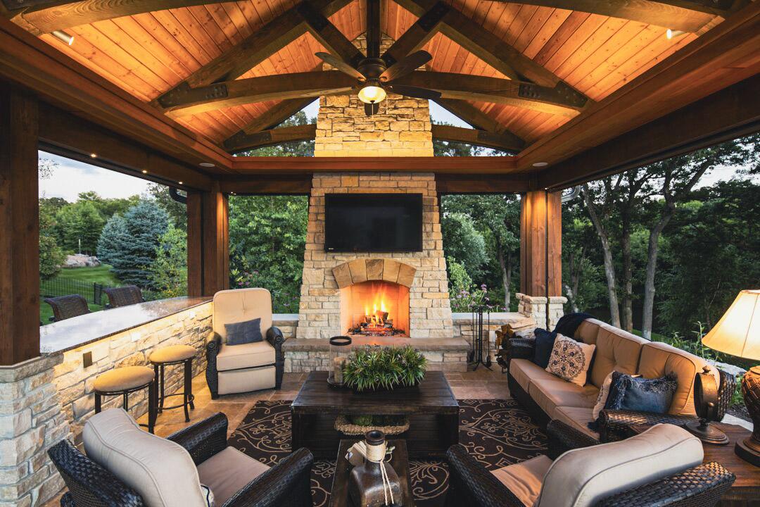 Covered outdoor living room with stone fireplace and wood ceiling