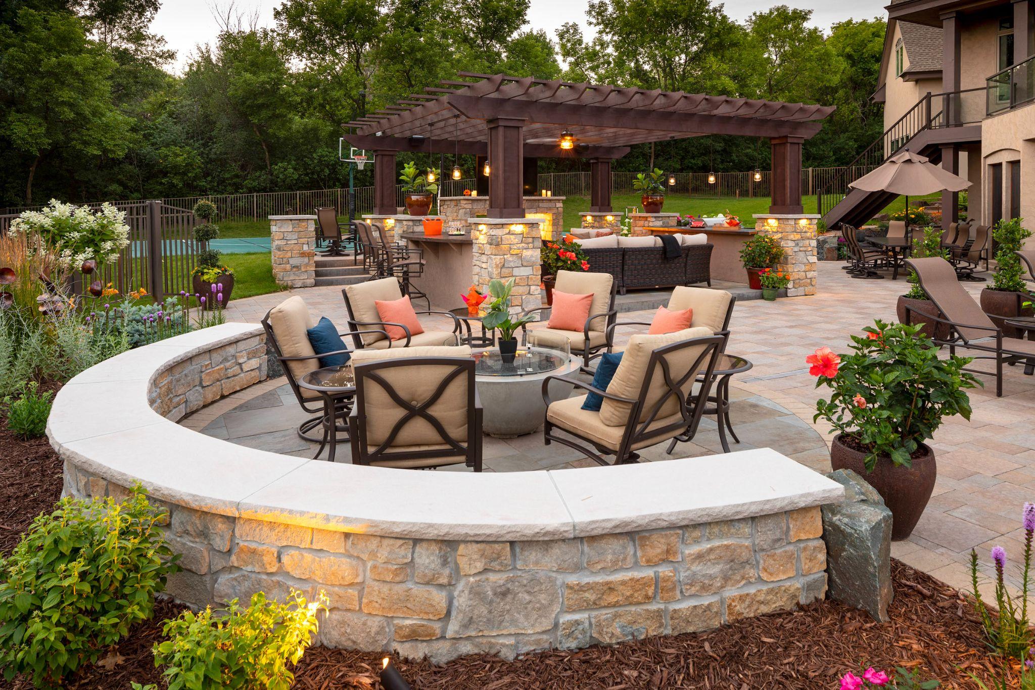 Curved stone fire pit seating area with pergola and paver patio at dusk