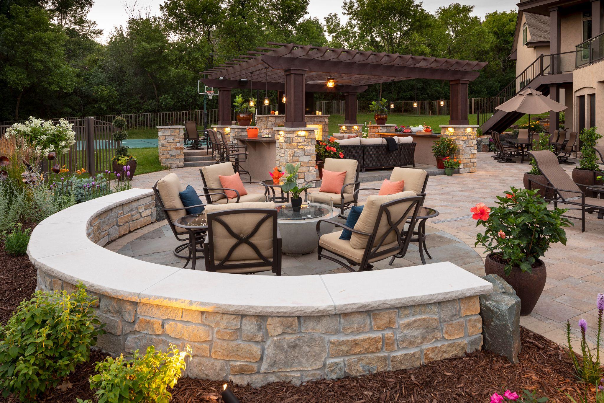 Curved stone seating wall around fire pit with paver patio and pergola at dusk