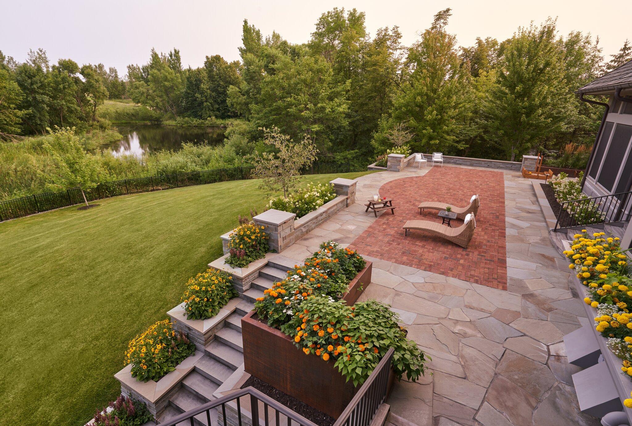 Multi-level flagstone and paver patio with tiered planters and lawn overlooking a pond