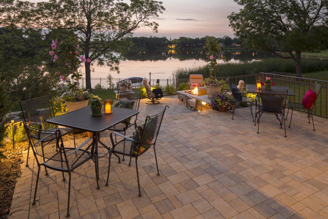 Paver patio with fire feature and dining area overlooking a lake at sunset