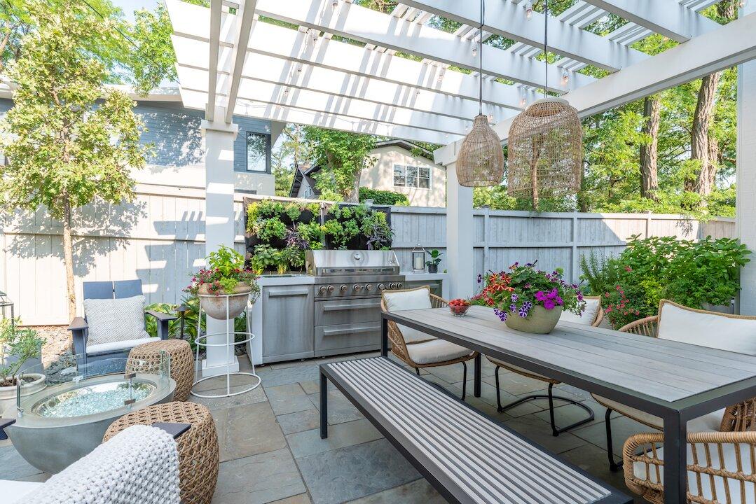White pergola over flagstone patio with outdoor kitchen, dining area, and fire bowl seating