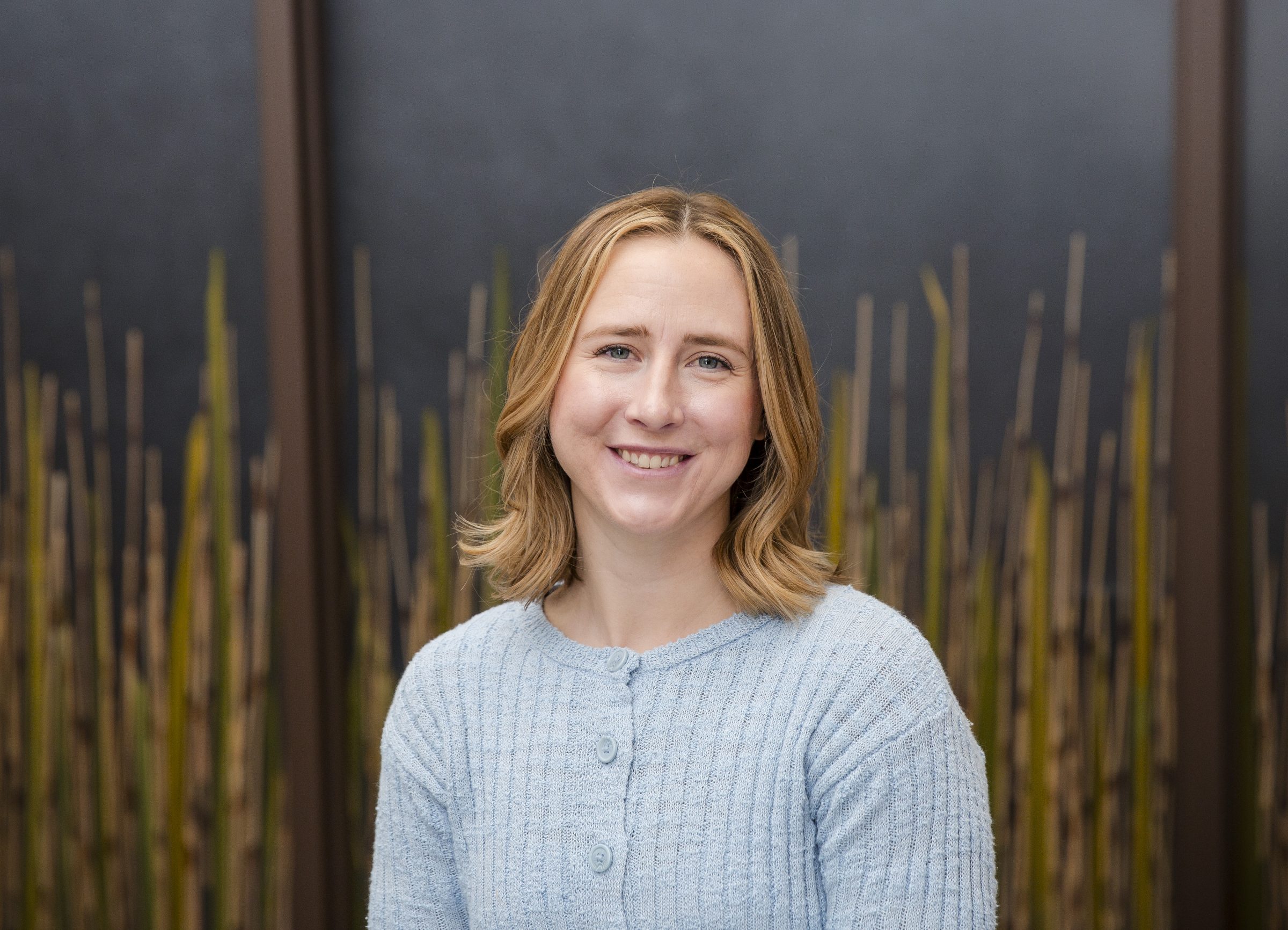 Smiling person in a blue sweater, bamboo background.