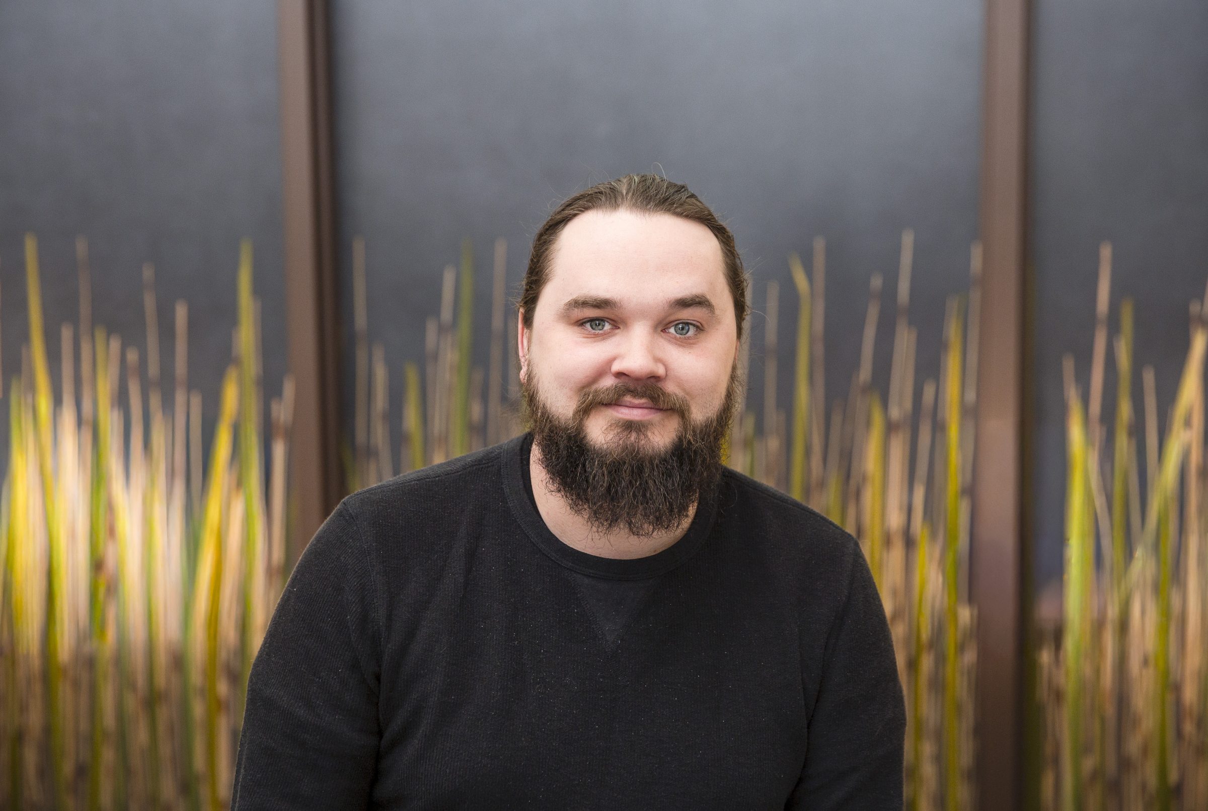 Person with beard smiling, bamboo background.