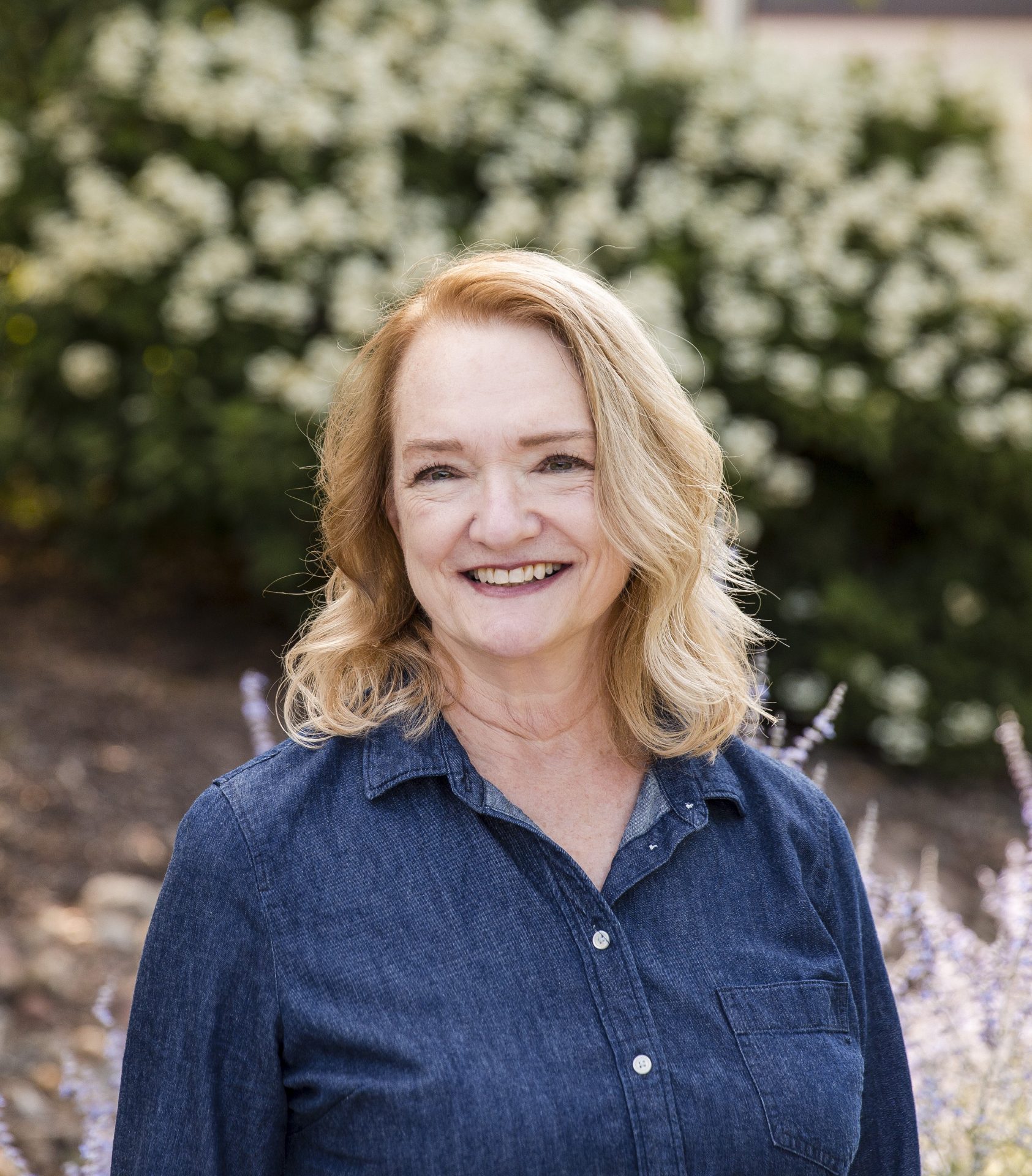 Smiling woman outdoors with blooming flowers background.