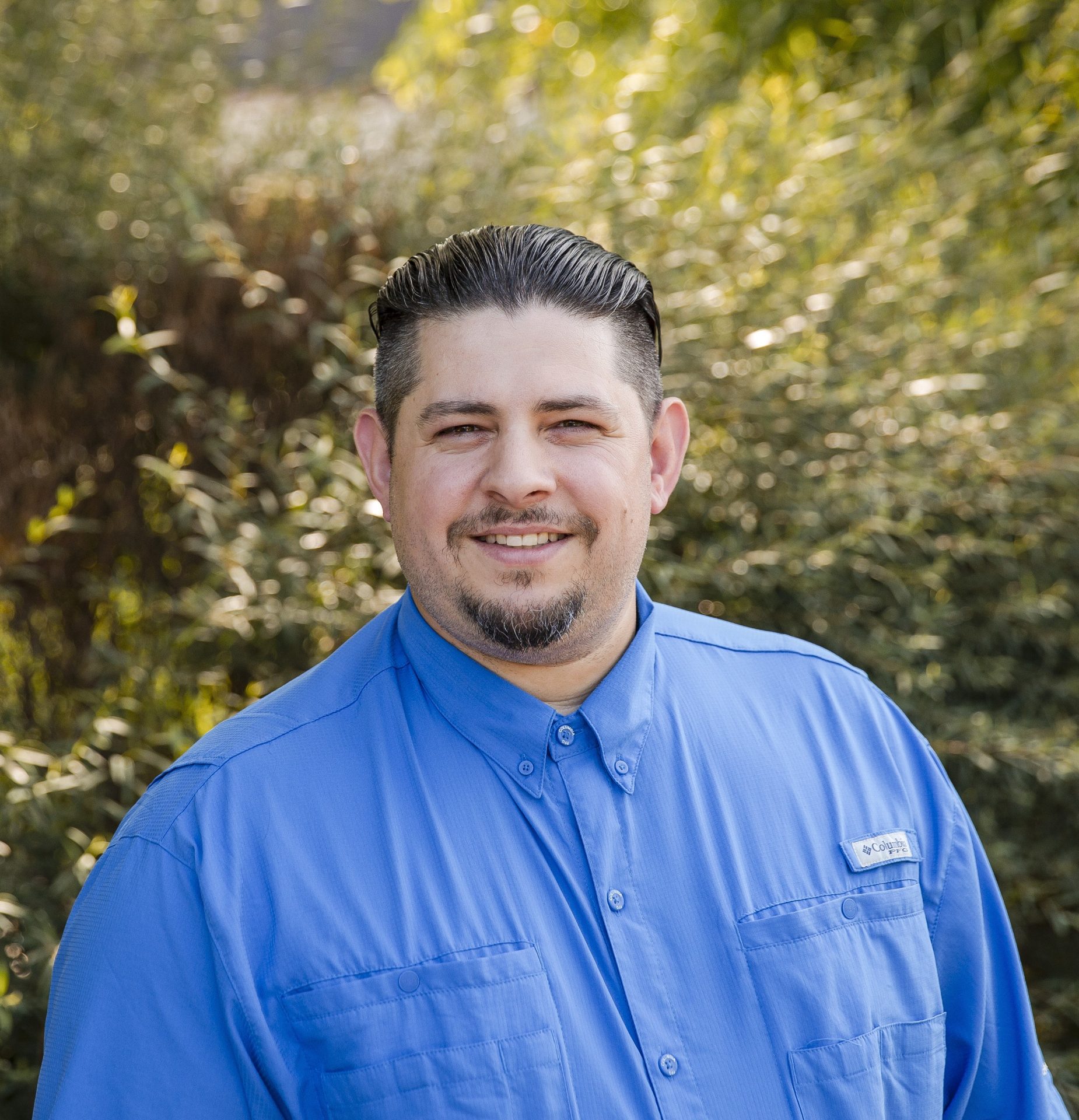 Smiling man in a blue shirt outdoors.