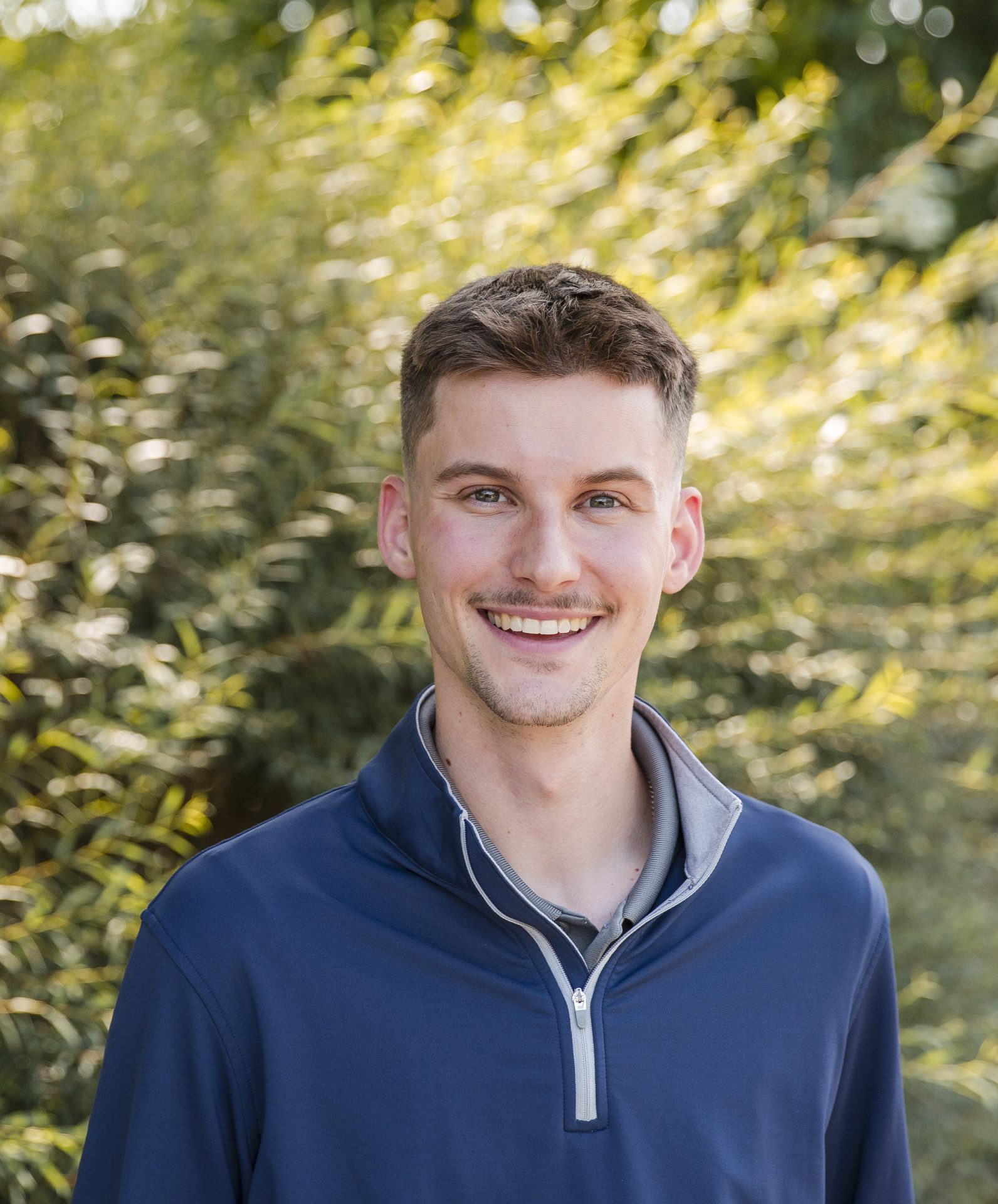 Smiling person outside with green foliage background.
