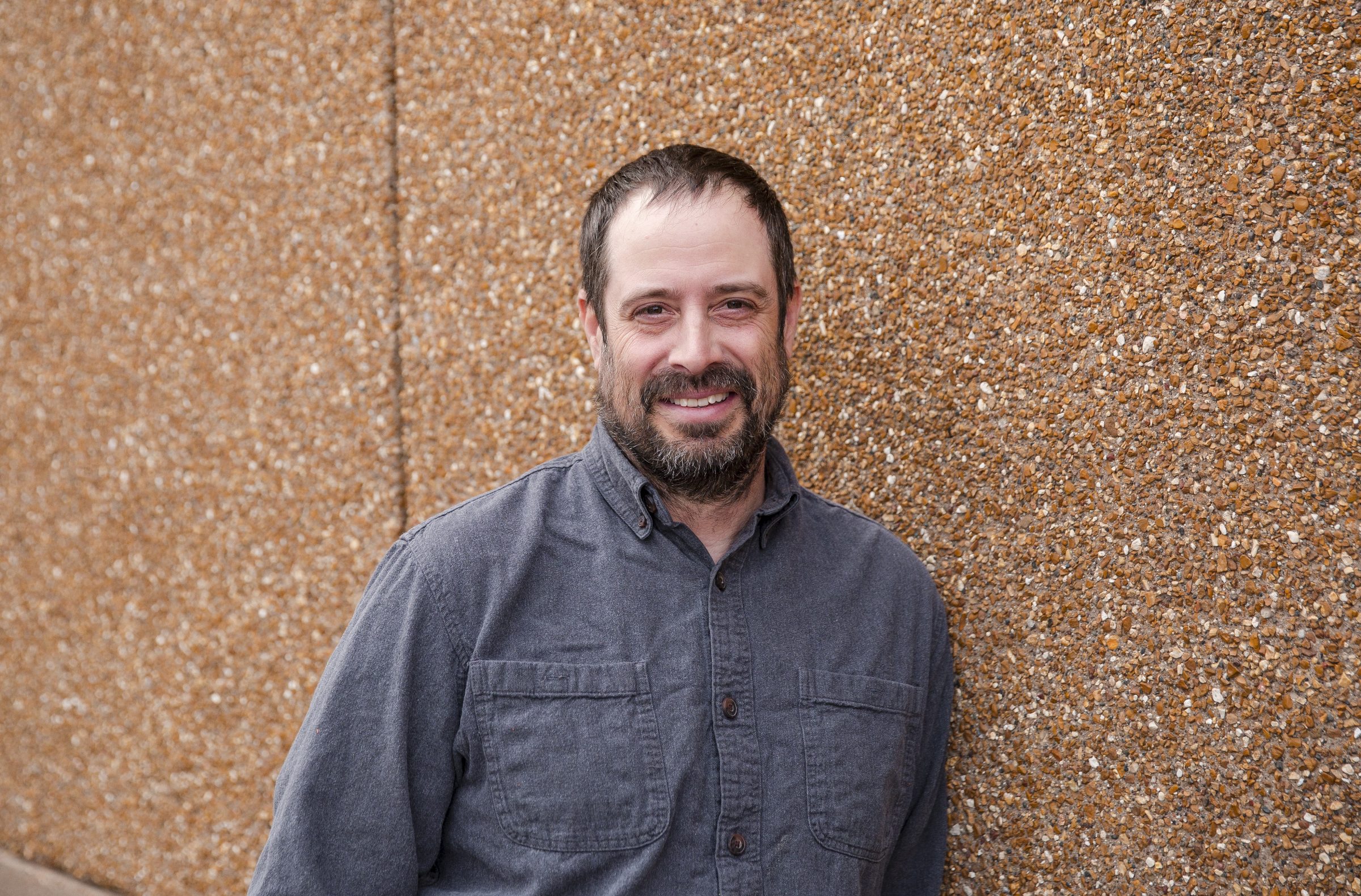 Smiling man leaning against textured wall.