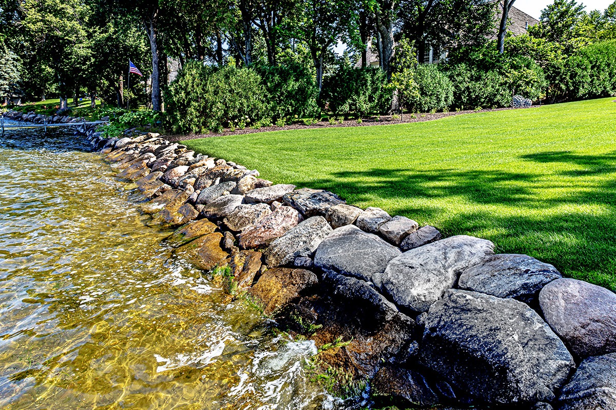 Rock-lined shoreline with lush green lawn.