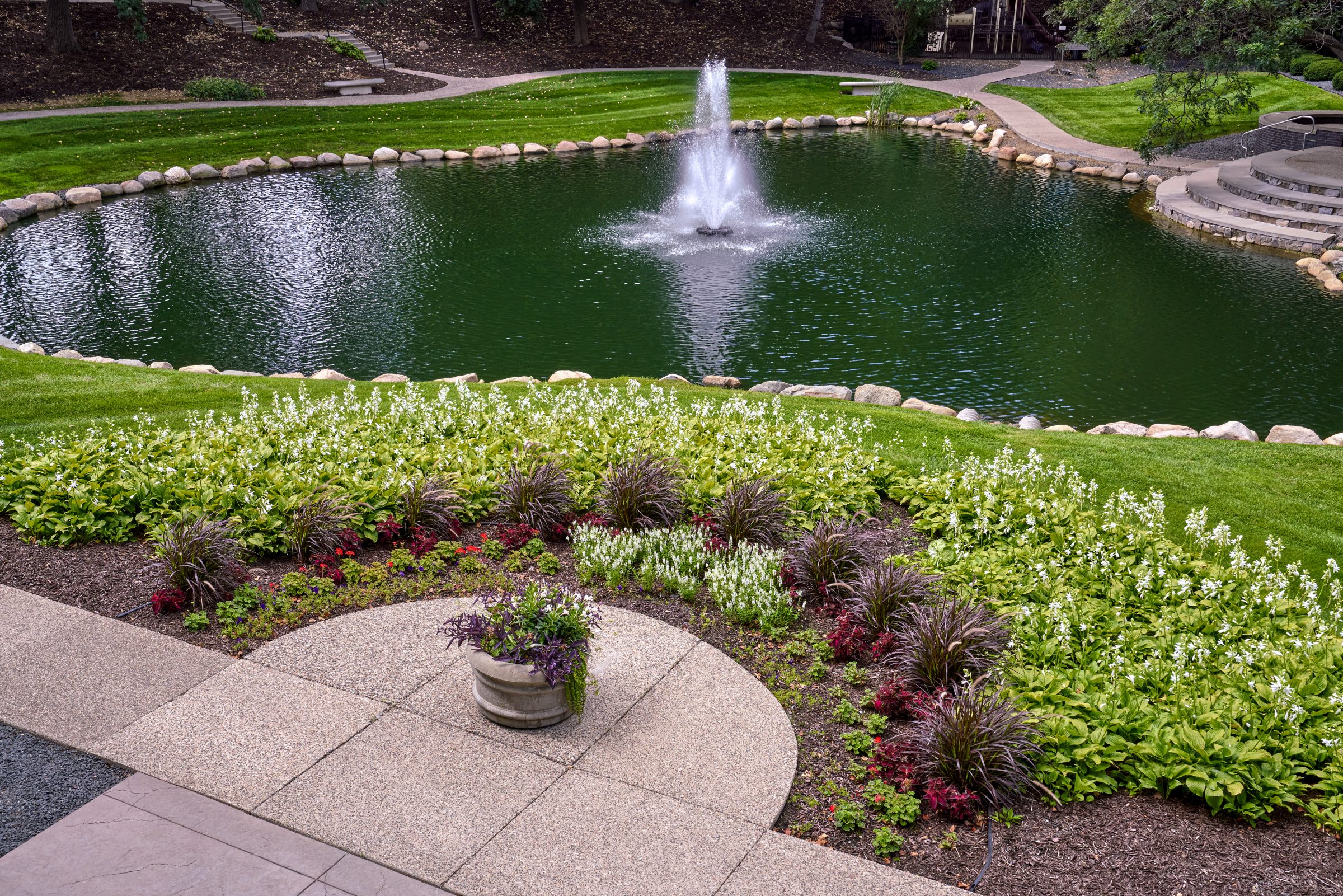 Fountain pond bordered by flowering plants and green lawn at Normandale Lakes Office Park