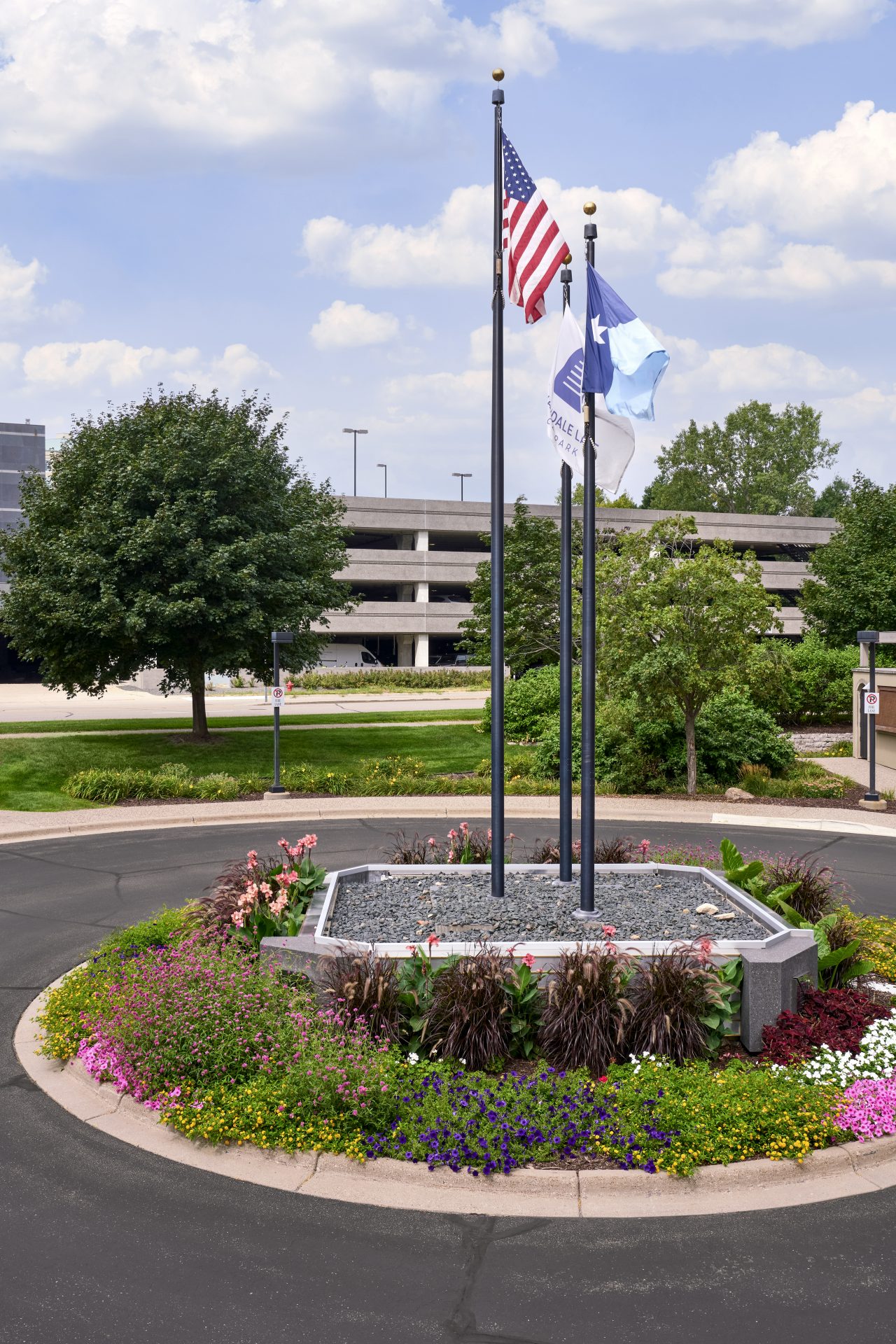 Three flags in landscaped roundabout with flowers.