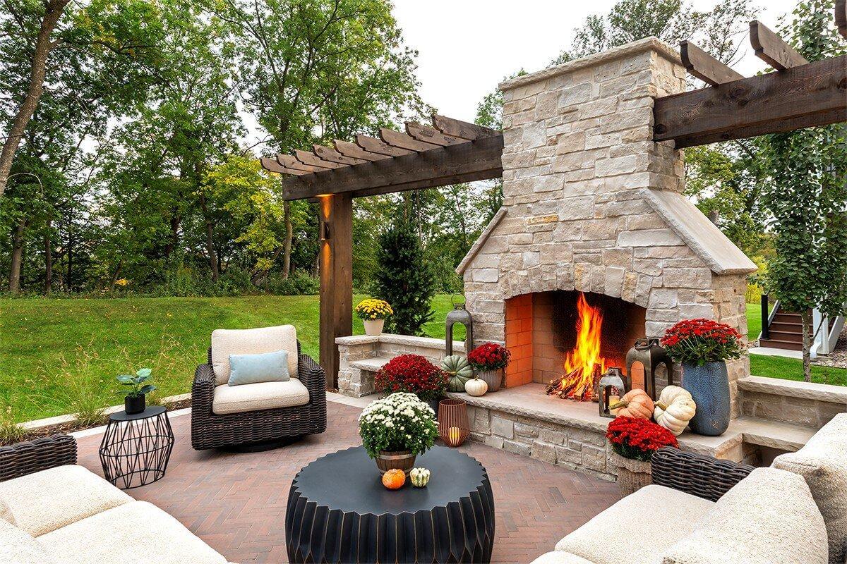 Autumn landscape design featuring a custom masonry outdoor fireplace, patio seating, and fall decor.