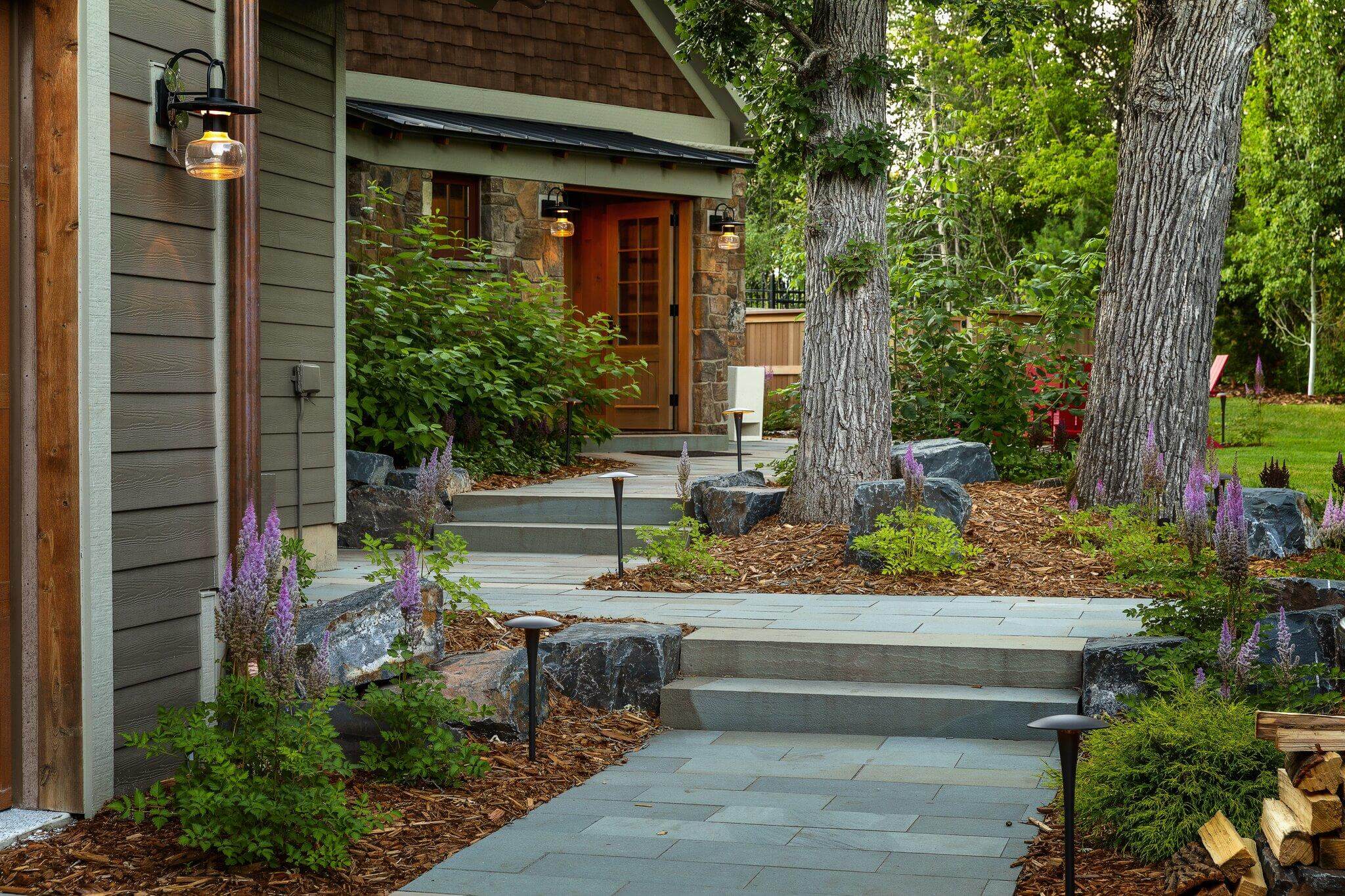 Bluestone walkway with stone steps, path lighting, and mature trees leading to home entrance.